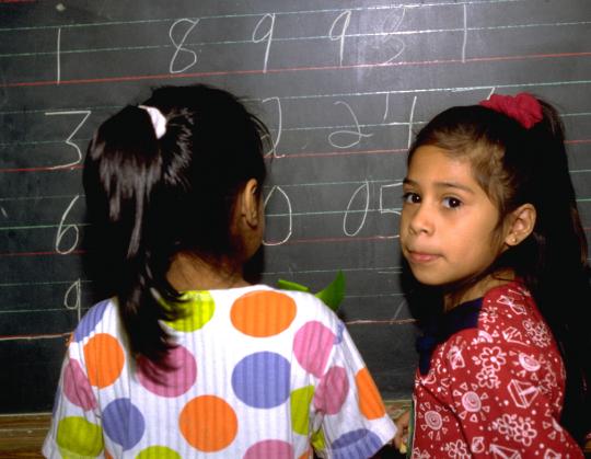 Elementary school bilingual Hispanic children adding big numbers on a chalkboard